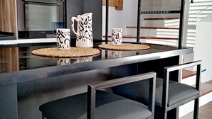 A modern kitchen with a black countertop, two bar stools, and a microwave. - Charme de L'atypique (Nabeul‎)