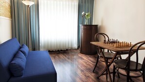 Une pièce avec un canapé bleu, une table d’échecs en bois et un meuble en bois foncé.