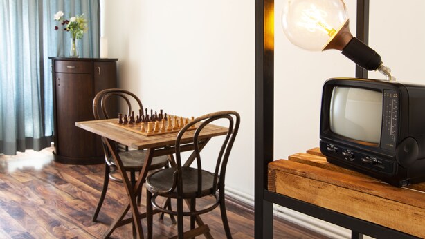 Une table en bois sur laquelle se trouvent un jeu d’échecs, un téléviseur ancien et une lampe posée sur un pied en bois.