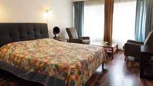 Une chambre d’hôtel avec un grand lit, deux fauteuils, une petite table et une lampe.