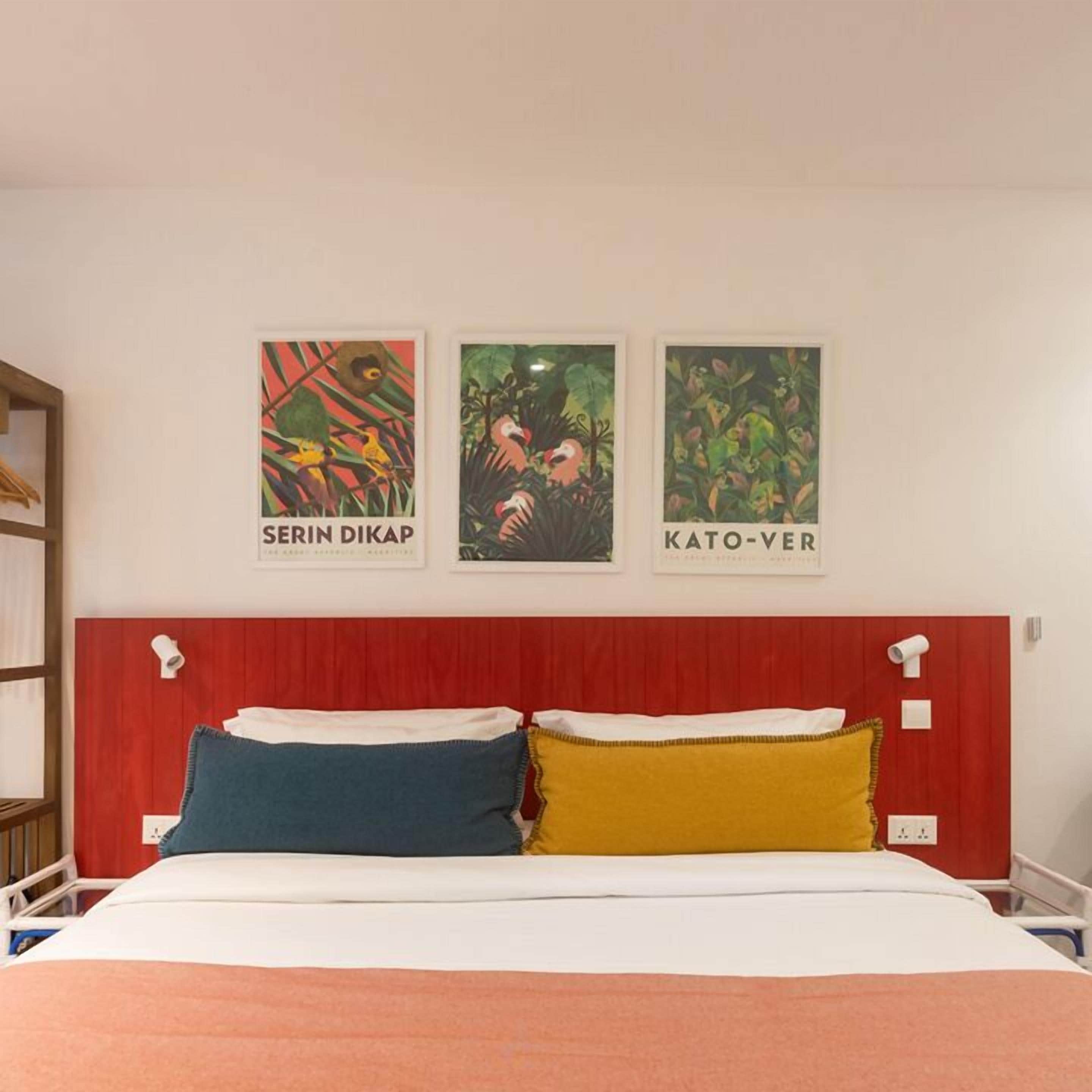 A hotel room with a red headboard, a bed with white and blue bedding, and three framed posters on the wall.