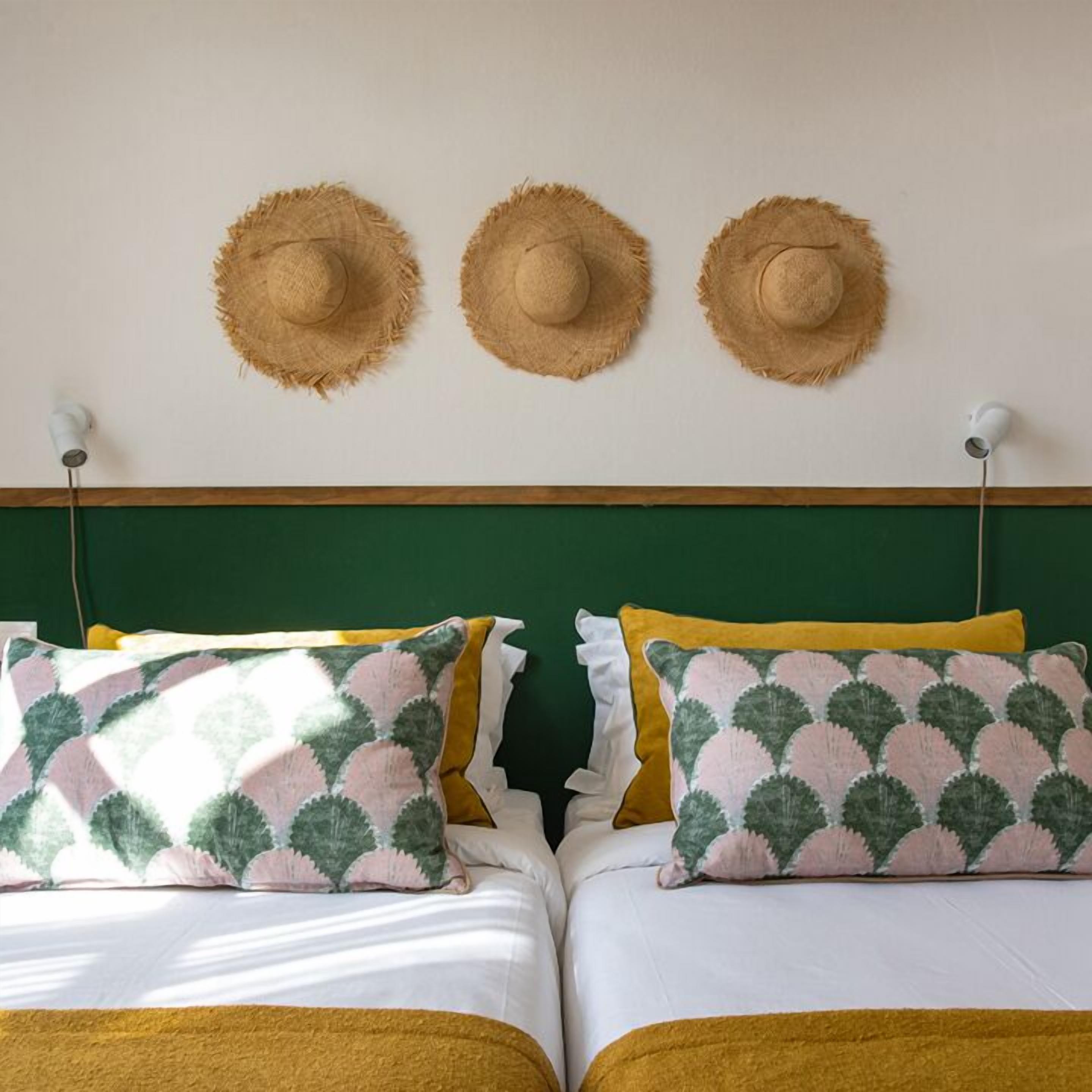 A double bed with two pillows, a green headboard, and three straw hats on the wall.