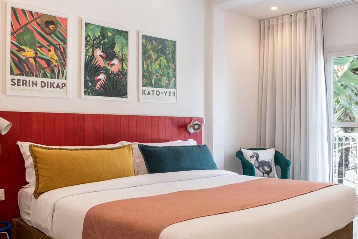 A hotel room with a bed, a red headboard, and three framed pictures on the wall.