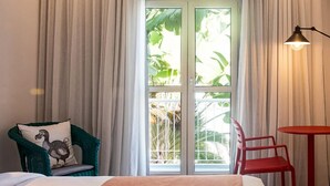 A hotel room with a bed, a chair, a small table, and a window with curtains. - Dodo Square (Grand-Baie)