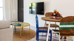 A modern living room with a sofa, a round coffee table, a blue chair, a wicker chair, a TV on the wall, and a ceiling fan. - Dodo Square (Grand-Baie)