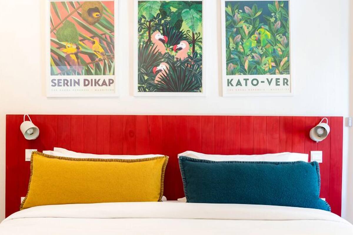 A bed with two pillows, a red headboard, and three framed artworks on the wall.