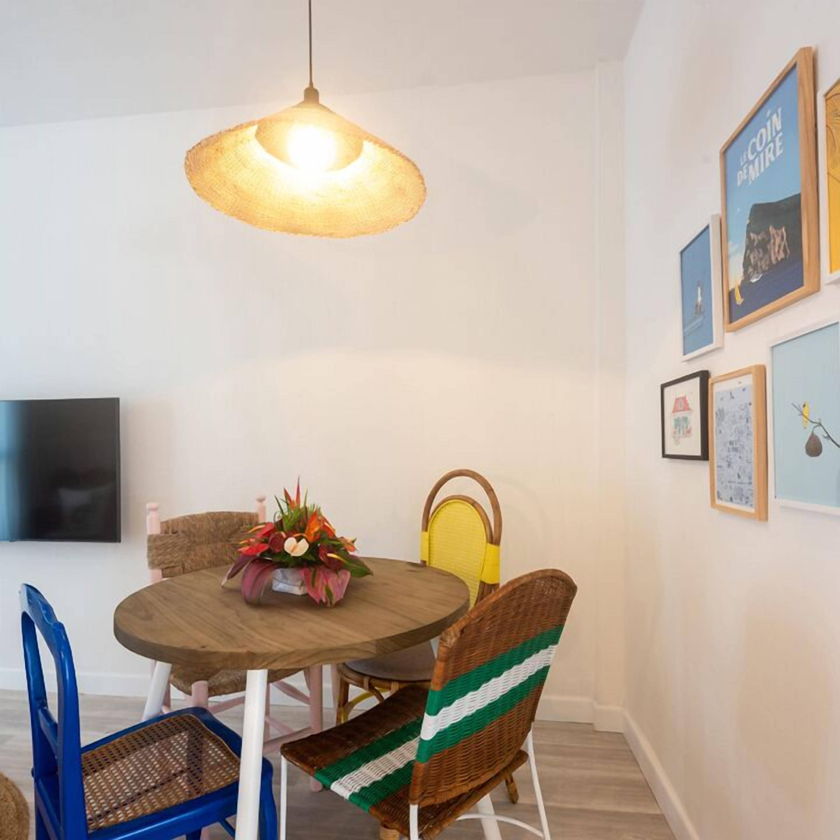 Un coin repas avec une table ronde, des chaises en osier et un luminaire suspendu.