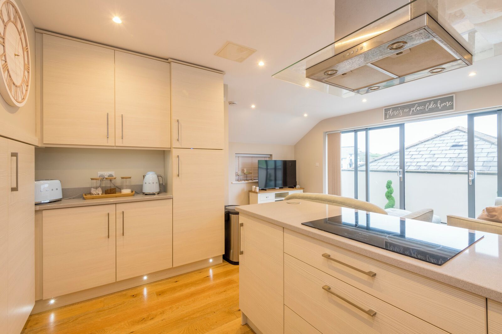 Une cuisine moderne avec des meubles de couleur bois clair, une cuisinière encastrée et une grande fenêtre donnant sur l’extérieur.