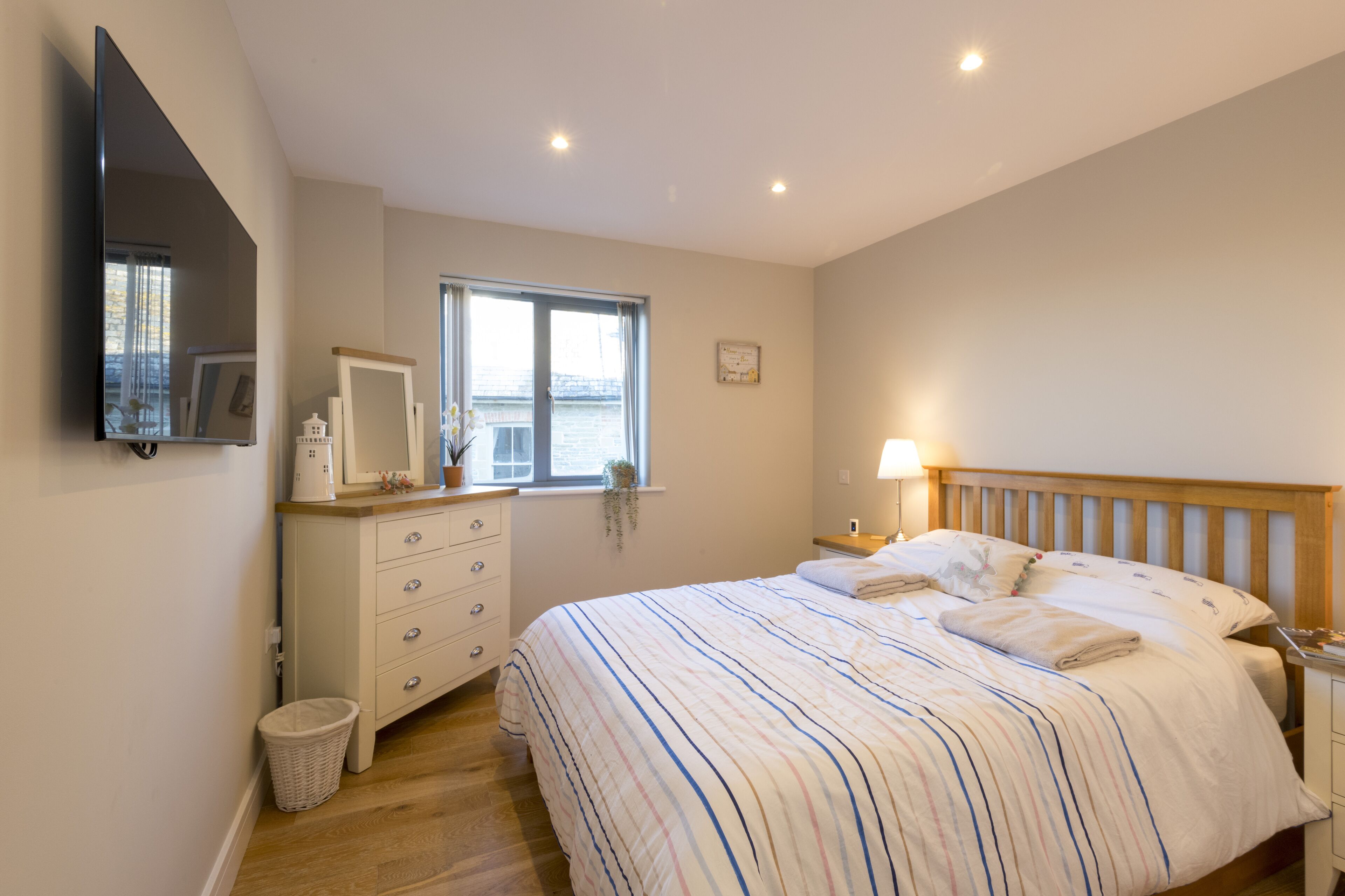 A bedroom with a bed, a dresser, a mirror, a TV, and a window.