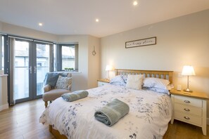 A bedroom with a large bed, two bedside tables with lamps, a wooden headboard, and a sliding glass door leading to a balcony.