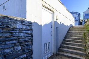 A white building with a stone wall and a set of concrete stairs leading up to a door.
