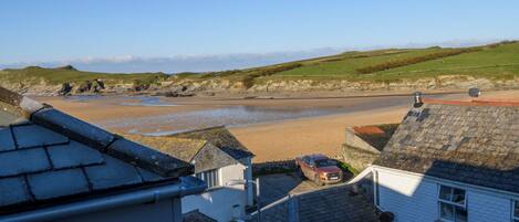 A coastal view with a sandy beach, a parked car, and white buildings with slate roofs.