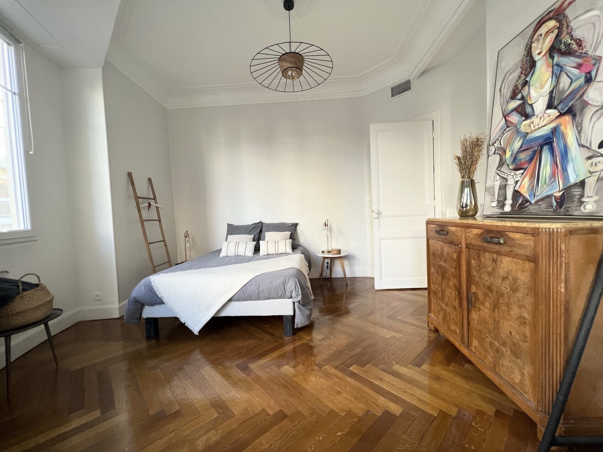 Une chambre à coucher avec un lit, un plancher en bois, une commode, un tableau et une échelle.