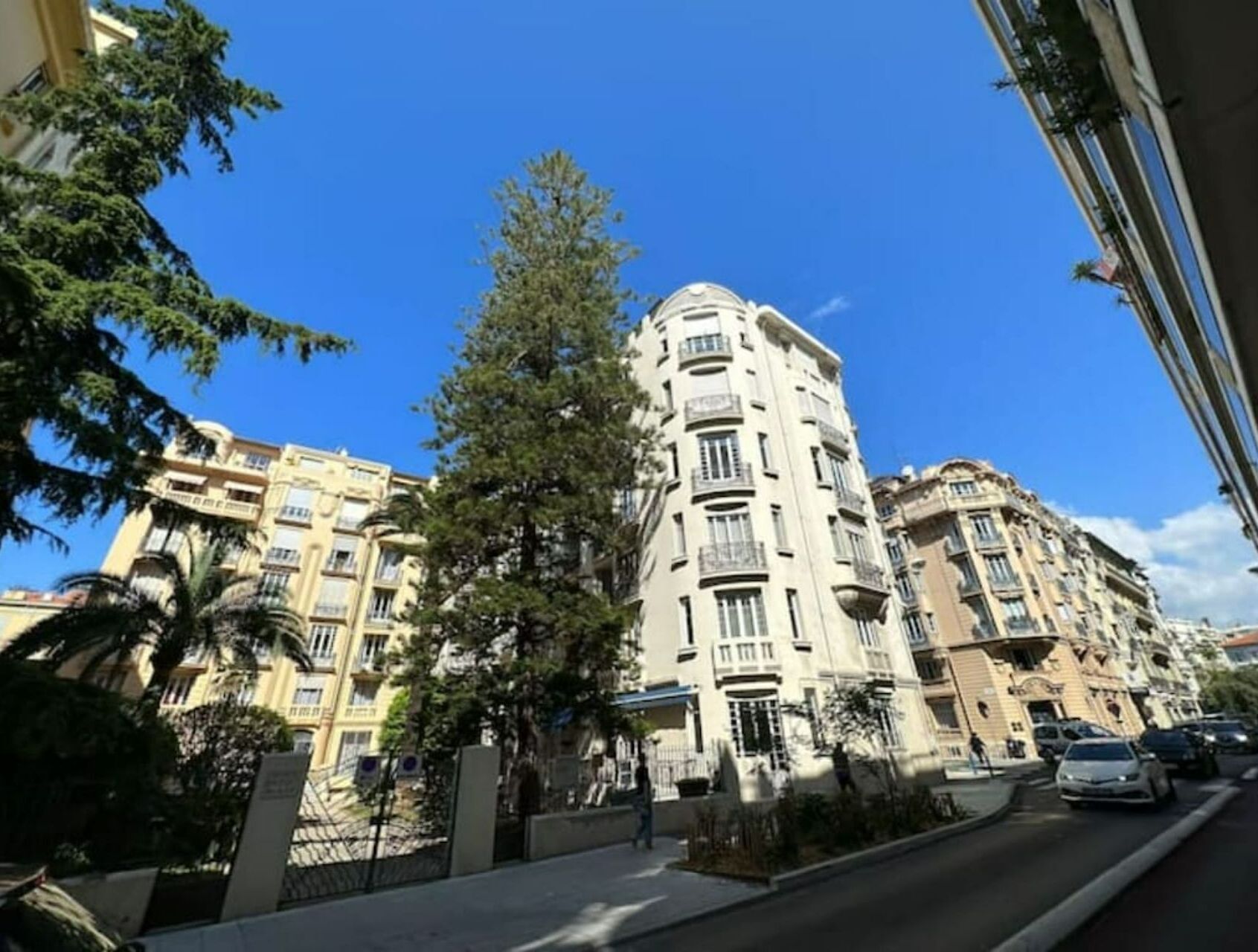Un edificio de varios pisos con balcones, rodeado de árboles y automóviles estacionados.