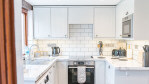 Une cuisine compacte avec des meubles blancs, un four encastré, un lave-linge et un grille-pain.