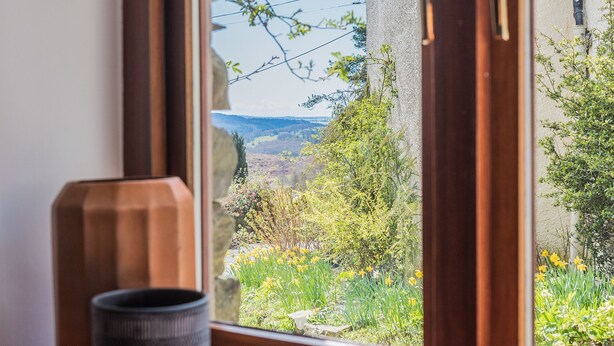 Une fenêtre donnant sur un jardin et un paysage lointain.