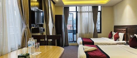 A hotel room with two beds, a TV, a table with water bottles, and a view of buildings through the window.