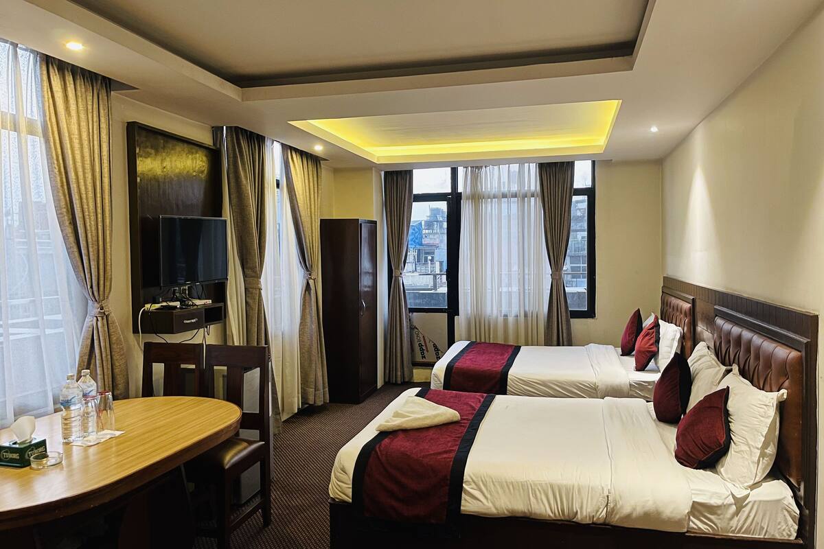 A hotel room with two beds, a desk, a TV, and a view of the city.