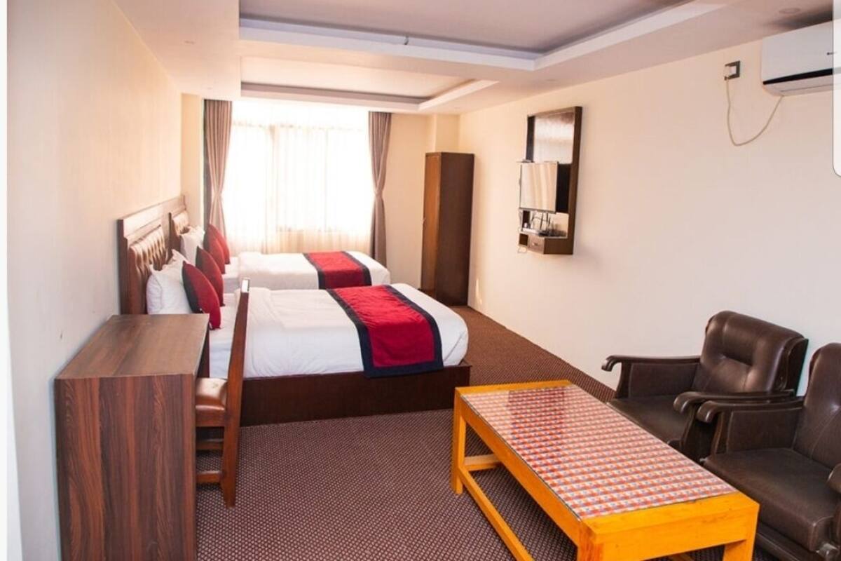 A hotel room with two beds, a desk, a chair, a table, and a mirror.