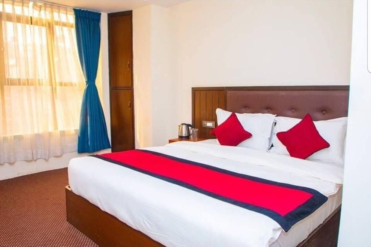 A hotel room with a large bed, a wooden headboard, and a red and white striped throw blanket.