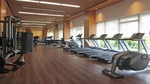 Un gimnasio con cintas de correr, máquinas de pesas y suelo de madera.