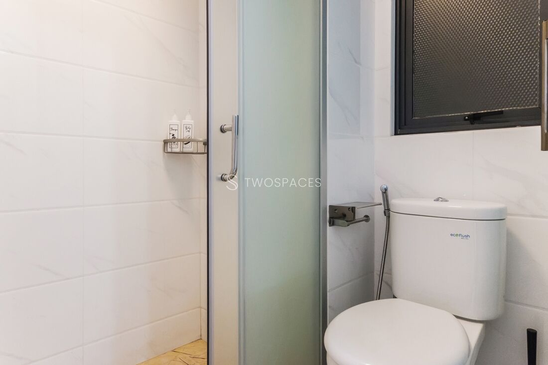 A modern bathroom with a glass shower enclosure, a toilet, and a small shelf with toiletries.