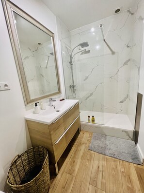 Ein modernes Badezimmer mit einer Marmerdusche, einem Holzanfang, einem großen Spiegel und einer kleinen Badewanne.