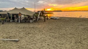 A beach with tents and beach chairs, a clear sky, and a sunset over the water. - Ferienhaus Holland-cube Direkt am Veluvemeer in Bad Hoophuizen (Hulshorst)