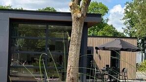 A modern building with large windows, a wooden deck, and outdoor seating. - Ferienhaus Holland-cube Direkt am Veluvemeer in Bad Hoophuizen (Hulshorst)