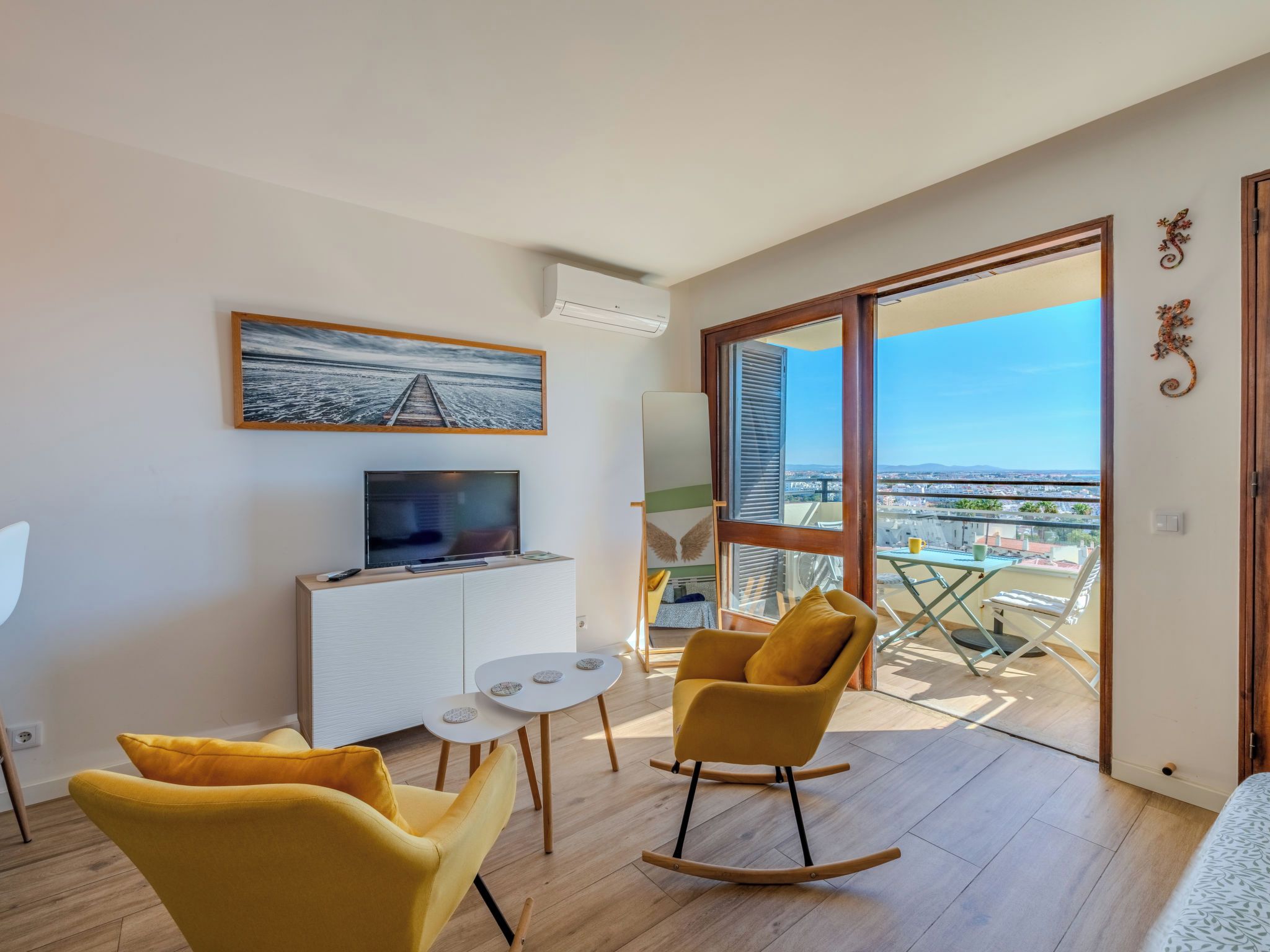 Uma sala de estar moderna com televisão, uma mesa pequena e cadeiras amarelas.