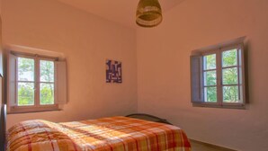 Une chambre à coucher comprenant un lit, deux fenêtres, un luminaire suspendu et une œuvre d’art accrochée au mur.