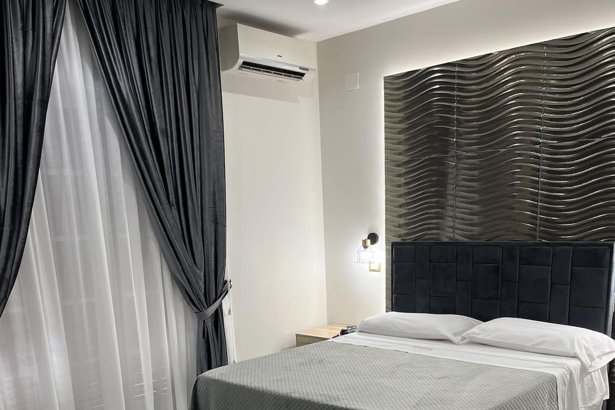 A modern bedroom with a large bed, a headboard with a textured design, a nightstand, and a chair.