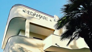 Ein modernes Gebäude, auf dem der Name 'REDDAMARE' gut sichtbar angebracht ist. Treppen führen zum Eingang, und das Gebäude zeichnet sich durch ein gebogenes Design aus.