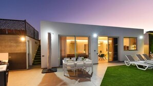 Une maison moderne dotée d’un patio comprenant une table et des chaises, une petite cuisine et une pelouse.