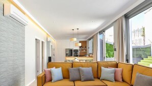Un salon moderne avec un canapé d’angle jaune, une table basse surmontée d’un globe terrestre et de télécommandes, et une cuisine en arrière-plan.