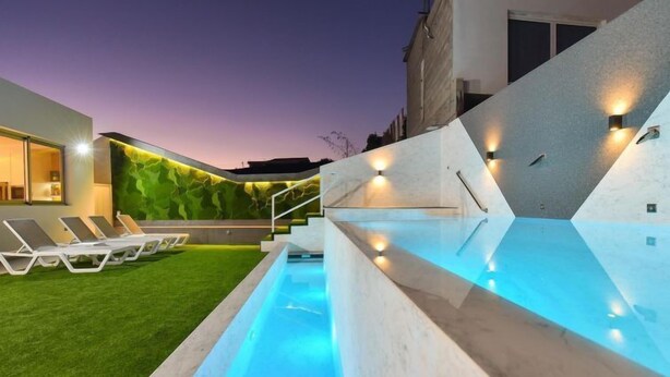 Une piscine extérieure moderne, dotée d’un design géométrique, entourée d’une pelouse bien entretenue et de chaises longues.