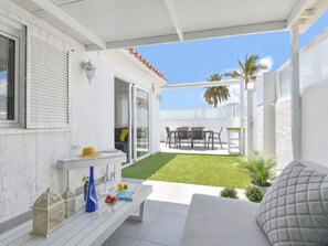 Eine moderne Terrasse mit weißer Fassade, einem grünen Rasen und einem Essbereich mit Gartenmöbeln.