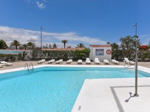 Una piscina con sillas reclinables blancas y una torre de salvavidas.