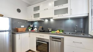 Una cocina moderna con armarios blancos, lavavajillas de acero inoxidable, horno, cafetera y fregadero.