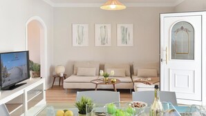 Una sala de estar moderna con un sofá, una mesa de centro y un televisor. Hay obras de arte enmarcadas en la pared y una puerta con ventana de vidrio.