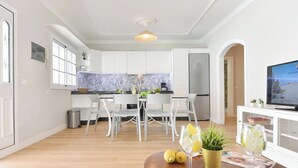 Una cocina moderna con armarios blancos, salpicadero de mármol y un comedor con sillas blancas.