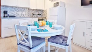 A modern kitchen with white cabinets, a built-in oven, and a refrigerator. There is a dining table with chairs and a bowl of fruit. - Comfortable Apartment with Attic in a Peaceful Village (Umag)