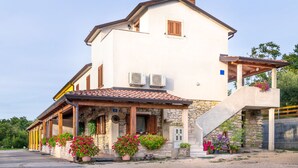 A two-story house with a stone facade, a tiled roof, and a covered porch with potted plants. - Comfortable Apartment with Attic in a Peaceful Village (Umag)