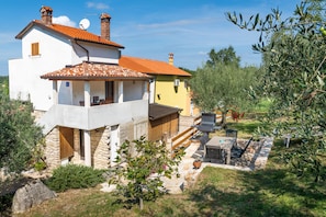 A two-story house with a stone facade, a tiled roof, and a small patio area with outdoor furniture. - Comfortable Apartment with Attic in a Peaceful Village (Umag)