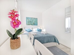 A minimalist bedroom with a bed, a bedside table, a potted orchid, and a painting on the wall. - Comfortable Apartment with Attic in a Peaceful Village (Umag)