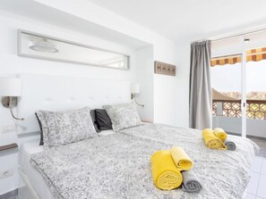 Habitación de hotel con una cama grande, dos almohadas, una mesita de noche, una lámpara de pared y un balcón con vistas.