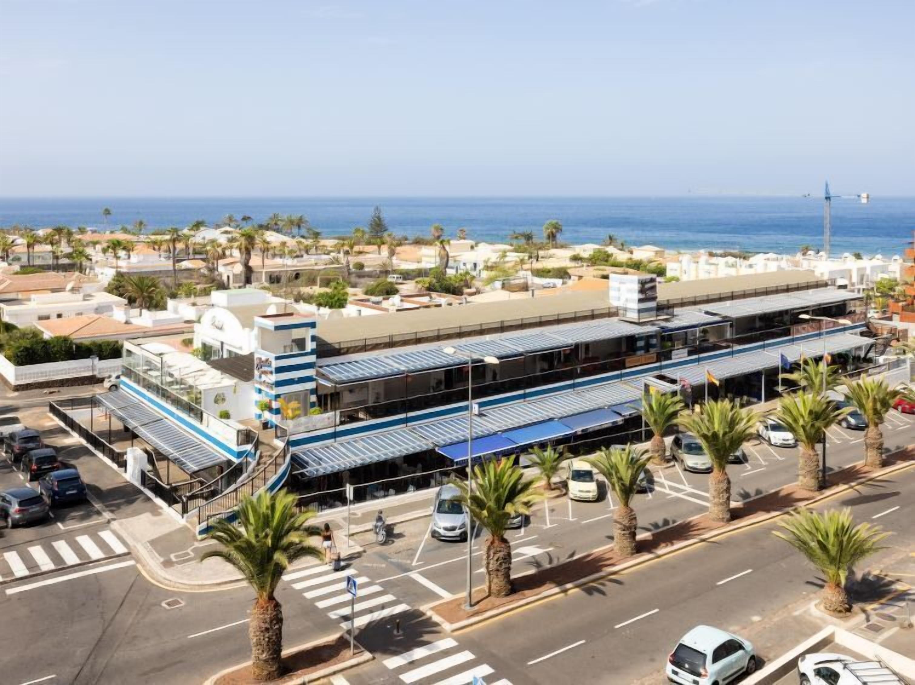 Vista aèria d'un hotel a la costa, amb aparcament, palmeres i vistes al mar.