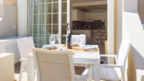 A sunlit patio with a table set for two, white chairs, and a view into the kitchen. - El Faro by Interhome (Palm- Mar)