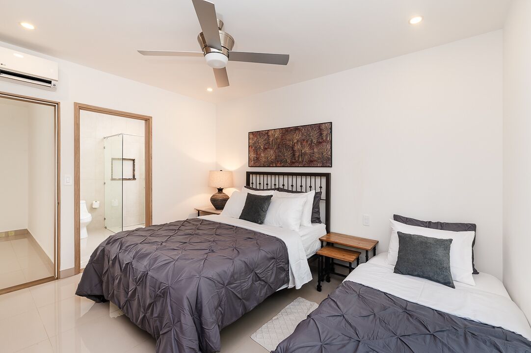 A modern bedroom with two beds, a ceiling fan, a bedside table with a lamp, and a large abstract painting on the wall.