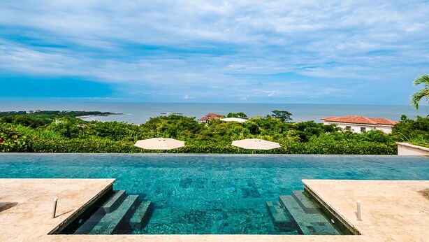 An infinity pool with a clear view of the ocean and a tropical landscape. - La Vista #B10, amazing Views - Brand New 3 bd Condo overlooking Tamarindo Bay Vista B-10 (Tamarindo)